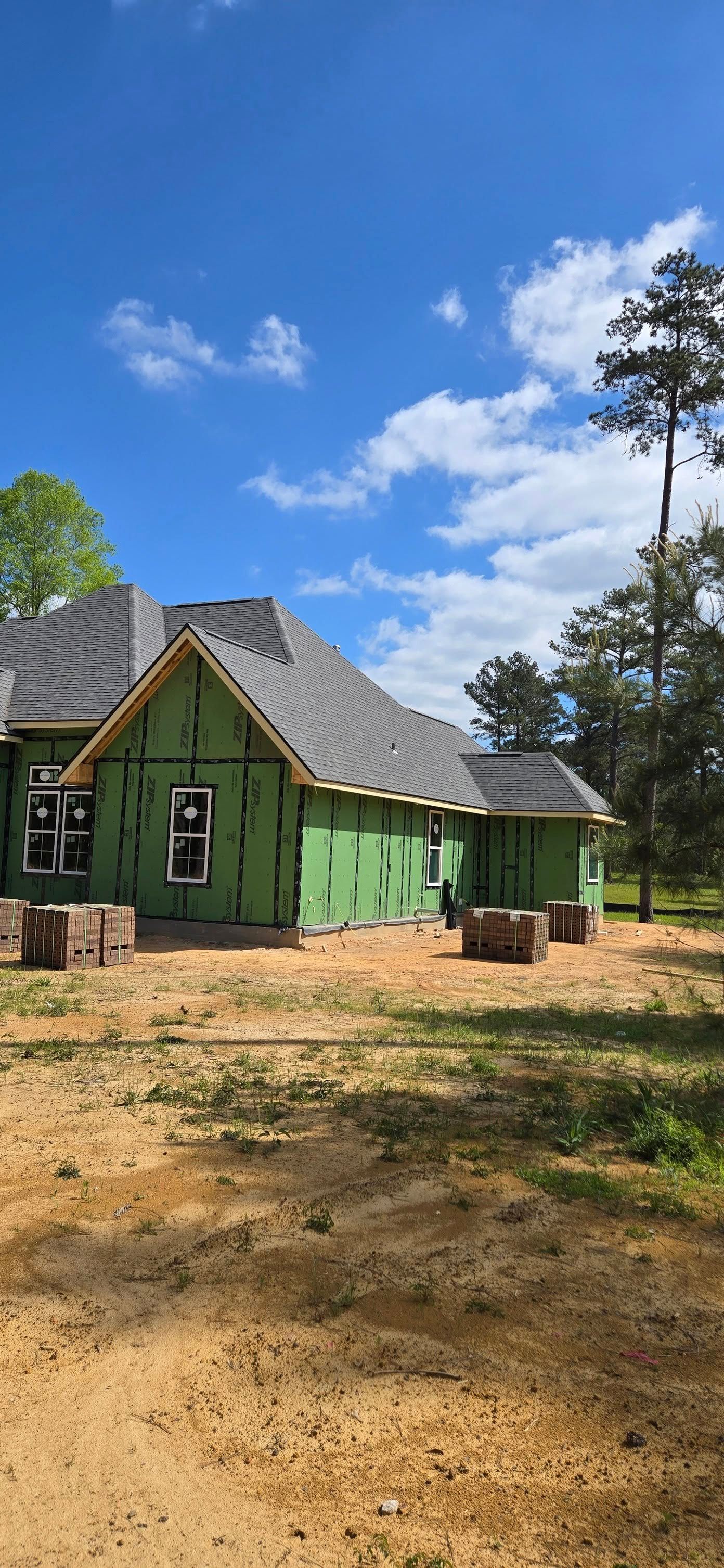 House under construction with green siding, gray roof, and blue sky.