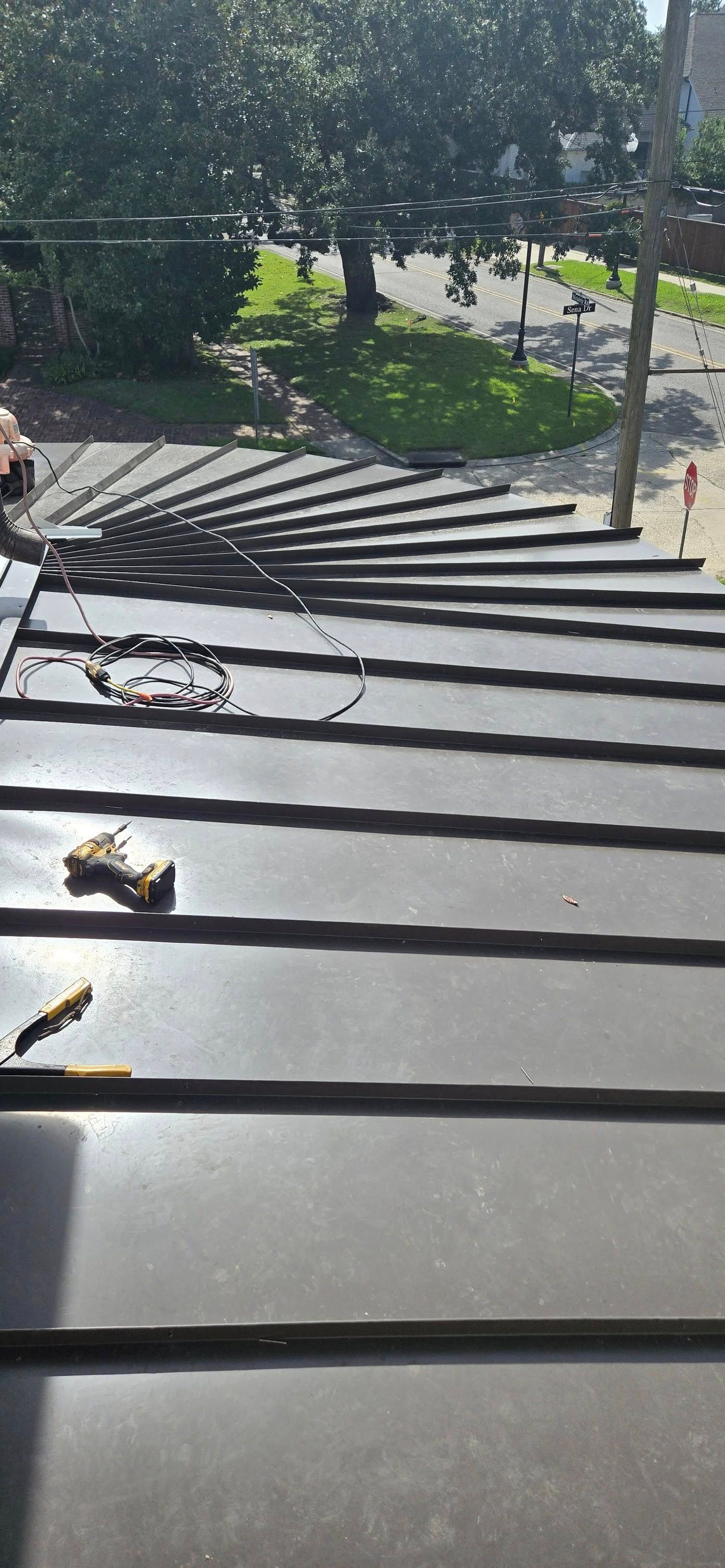 View from above of a dark, metal roof with a tree and a lawn in the background.
