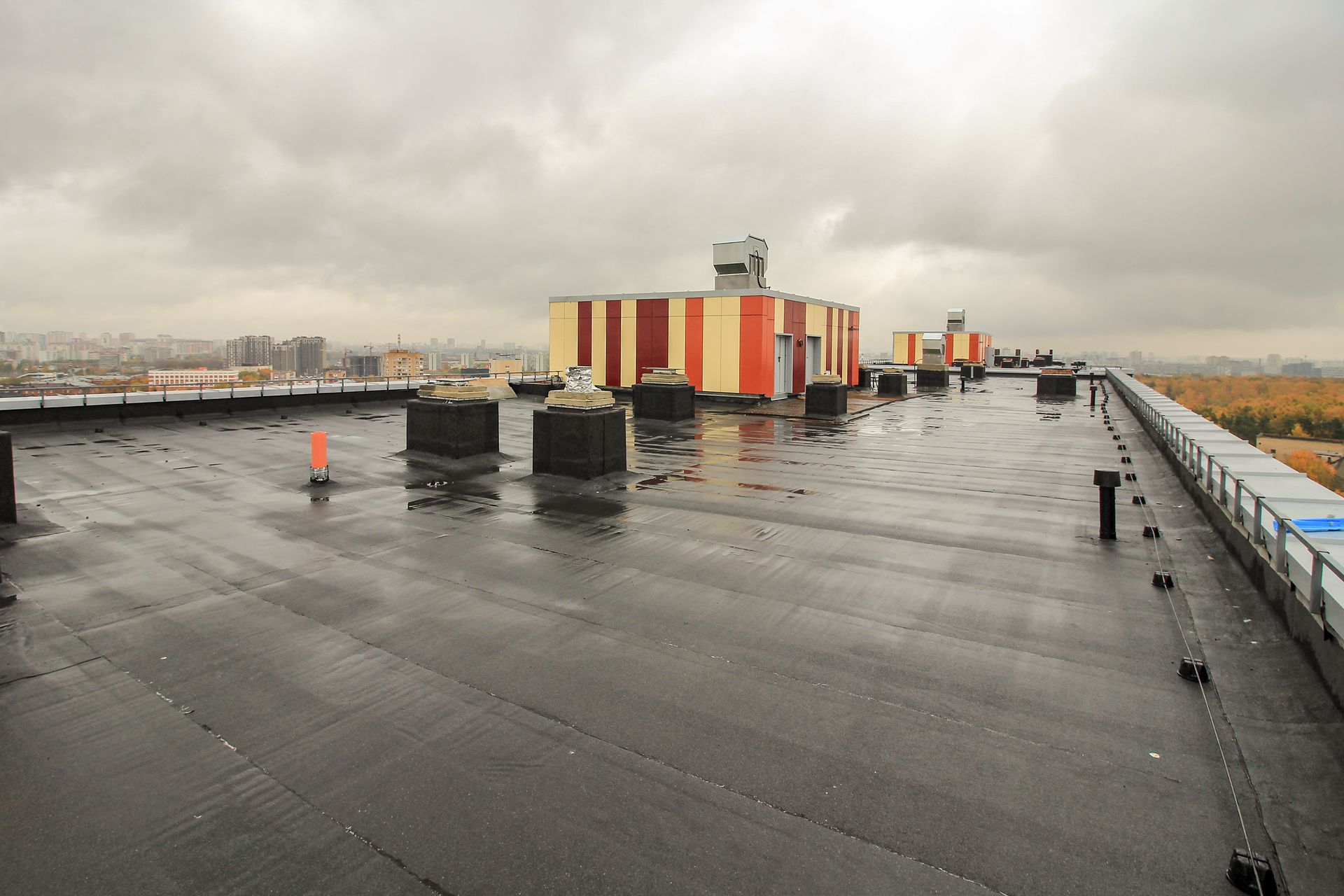 Flat, black rooftop on a building with utility structures, against a gray sky.