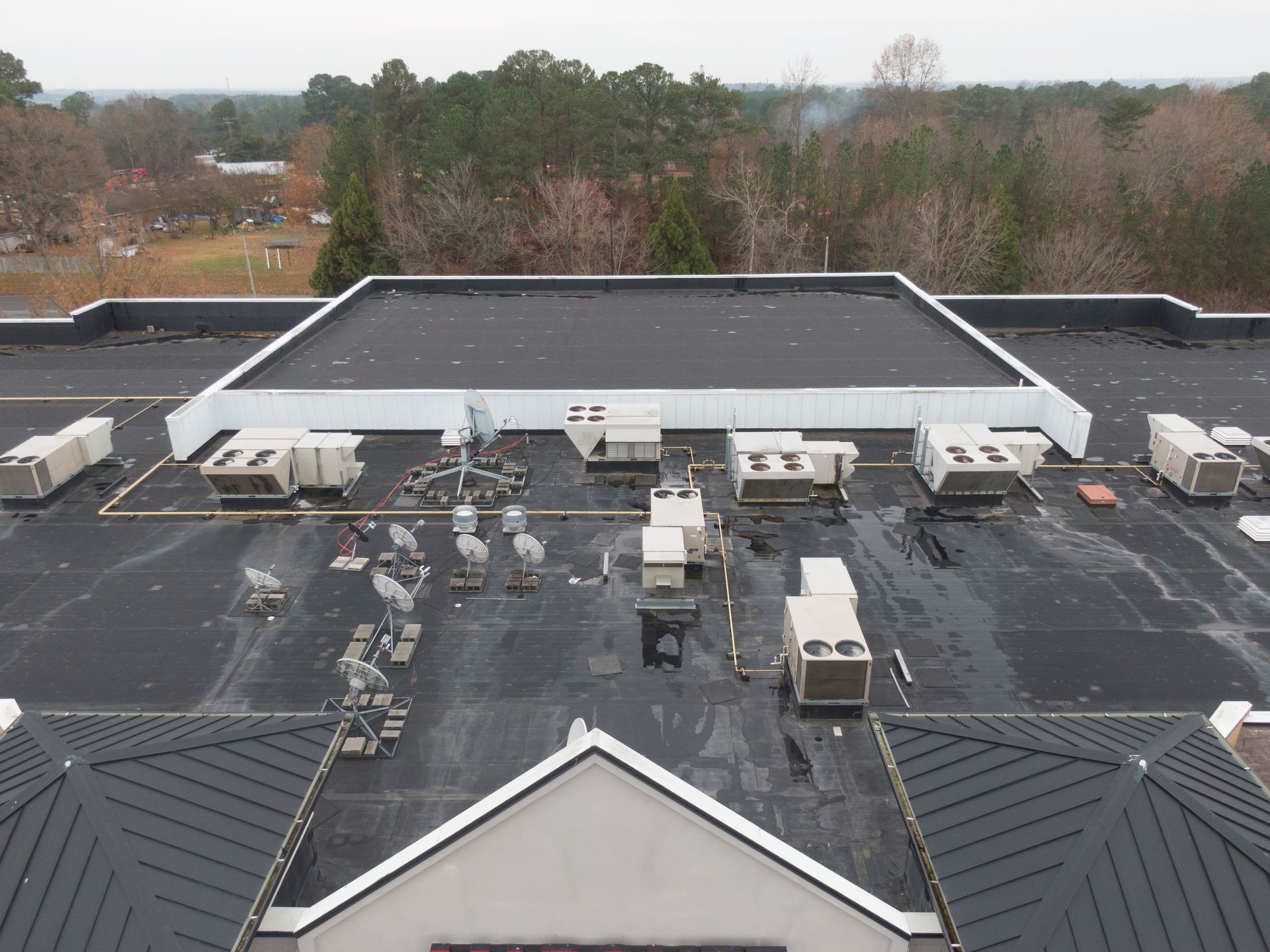 Rooftop of a building with HVAC units, black roof, and trees in the background.