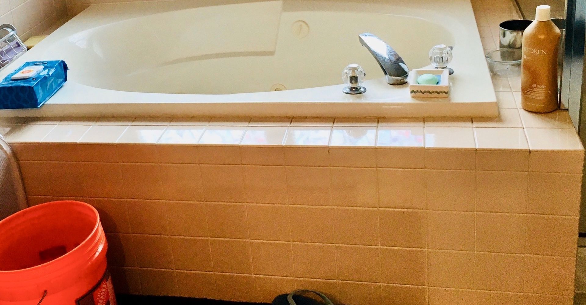 A bathtub in a bathroom with a bucket next to it.