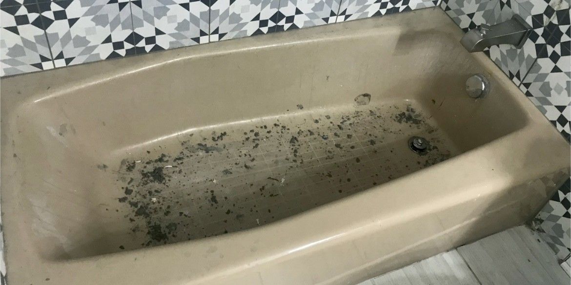 A dirty bathtub in a bathroom with a checkered wall.