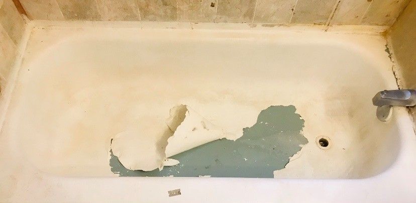 A bathtub with peeling paint on the floor in a bathroom.