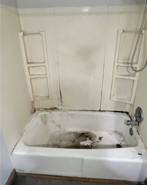 A dirty bathtub in a bathroom next to a shower.