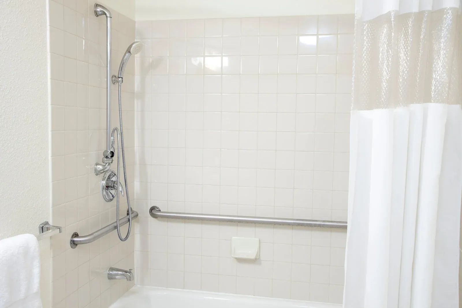 A bathroom with a tub , shower , and handrails.