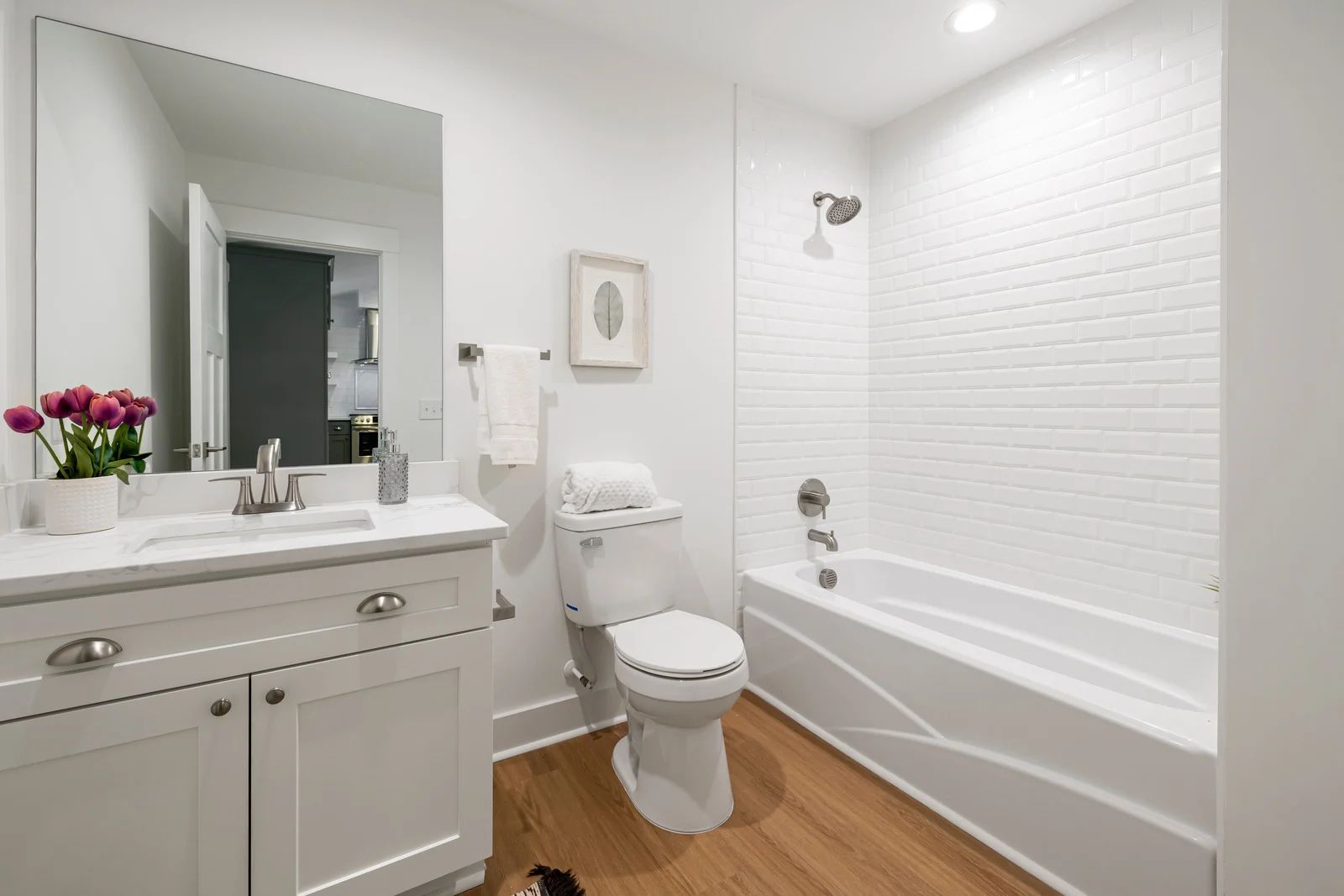 White bathroom with a vanity, toilet, and bathtub. Wooden floor.