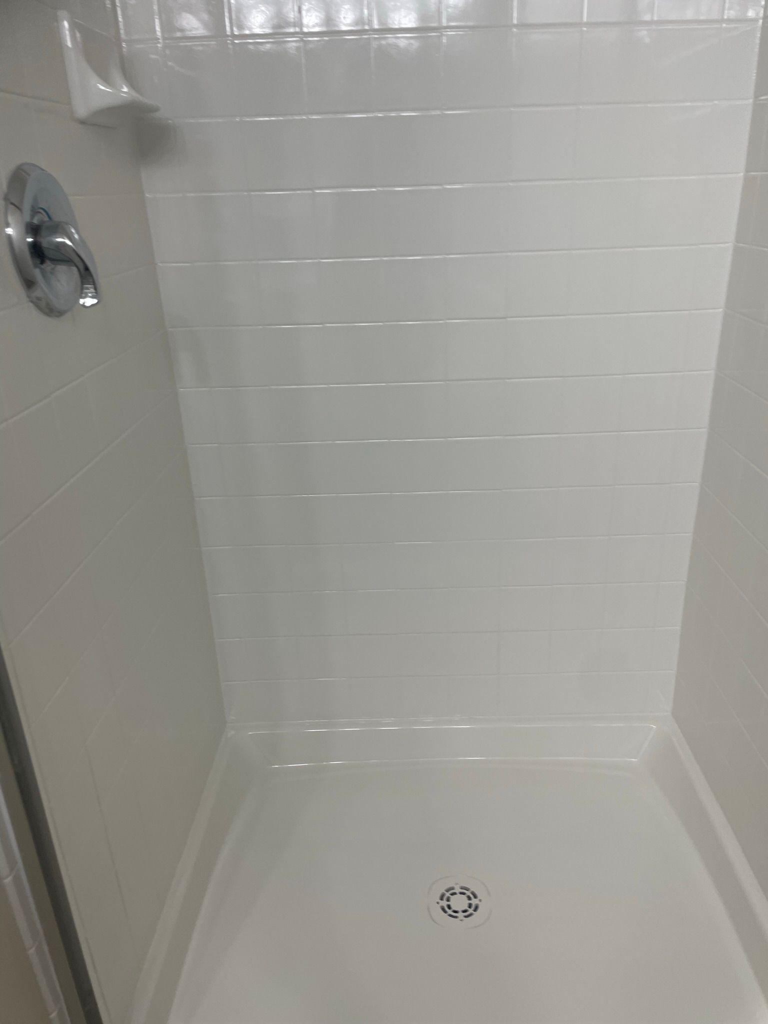 A shower stall with white tile walls and a drain.