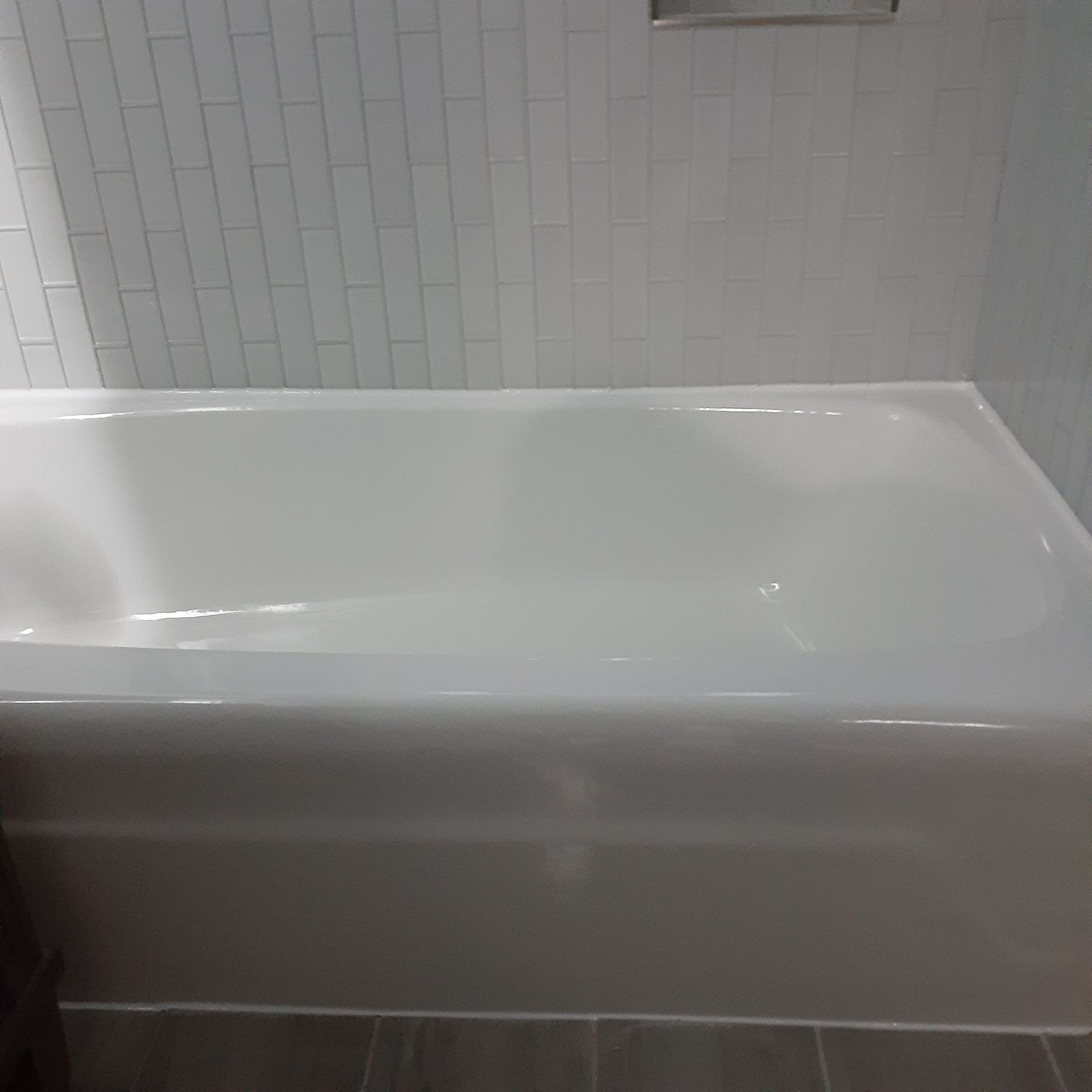 A white bathtub is sitting in a bathroom next to a white tiled wall.