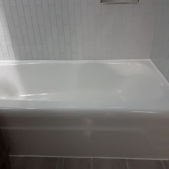 A white bathtub is sitting in a bathroom next to a white tiled wall.