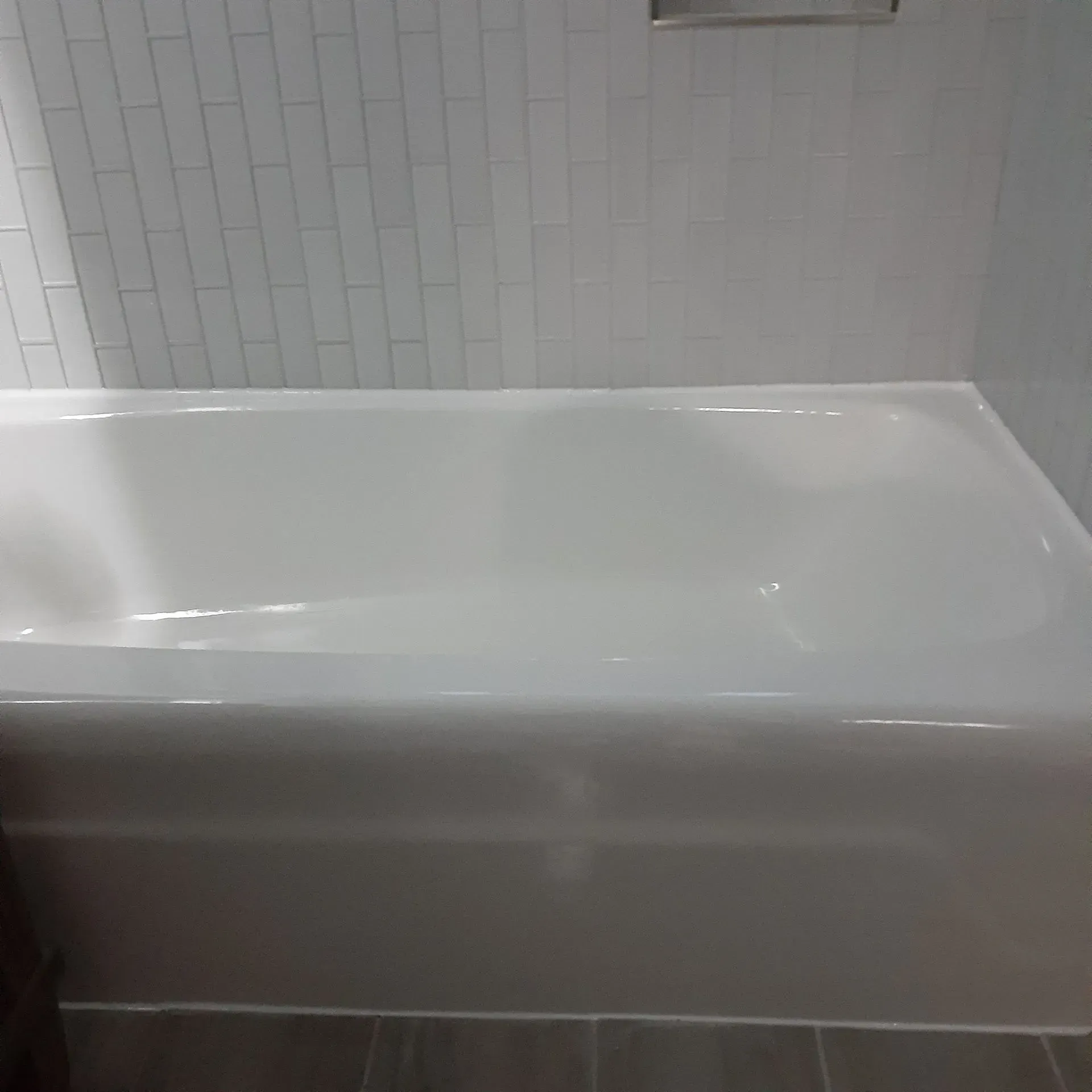 A white bathtub is sitting in a bathroom next to a white tiled wall.
