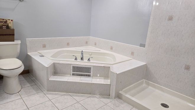 A bathroom with a jacuzzi tub , toilet and shower.