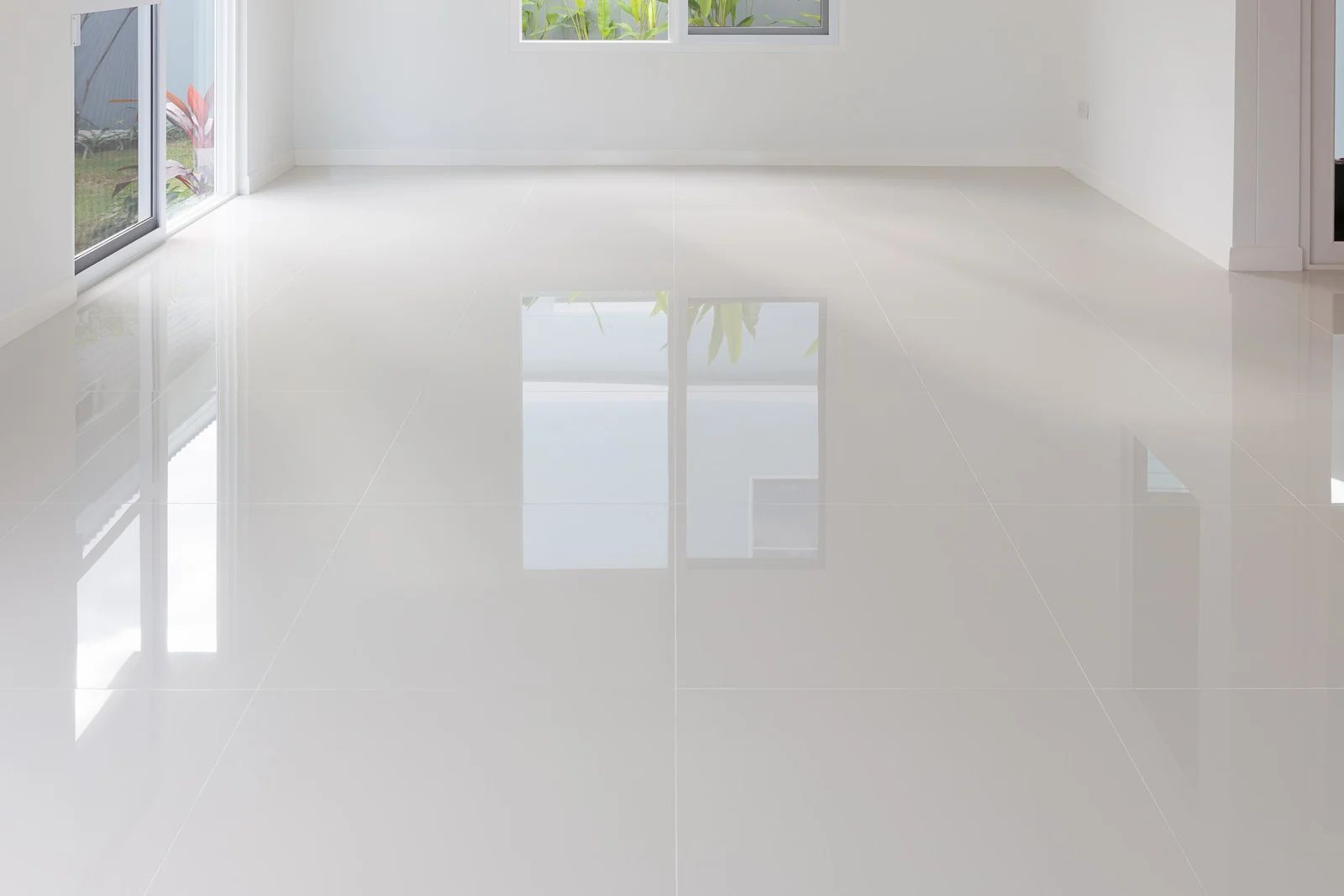 Empty room with glossy white tile floor reflecting light from windows.