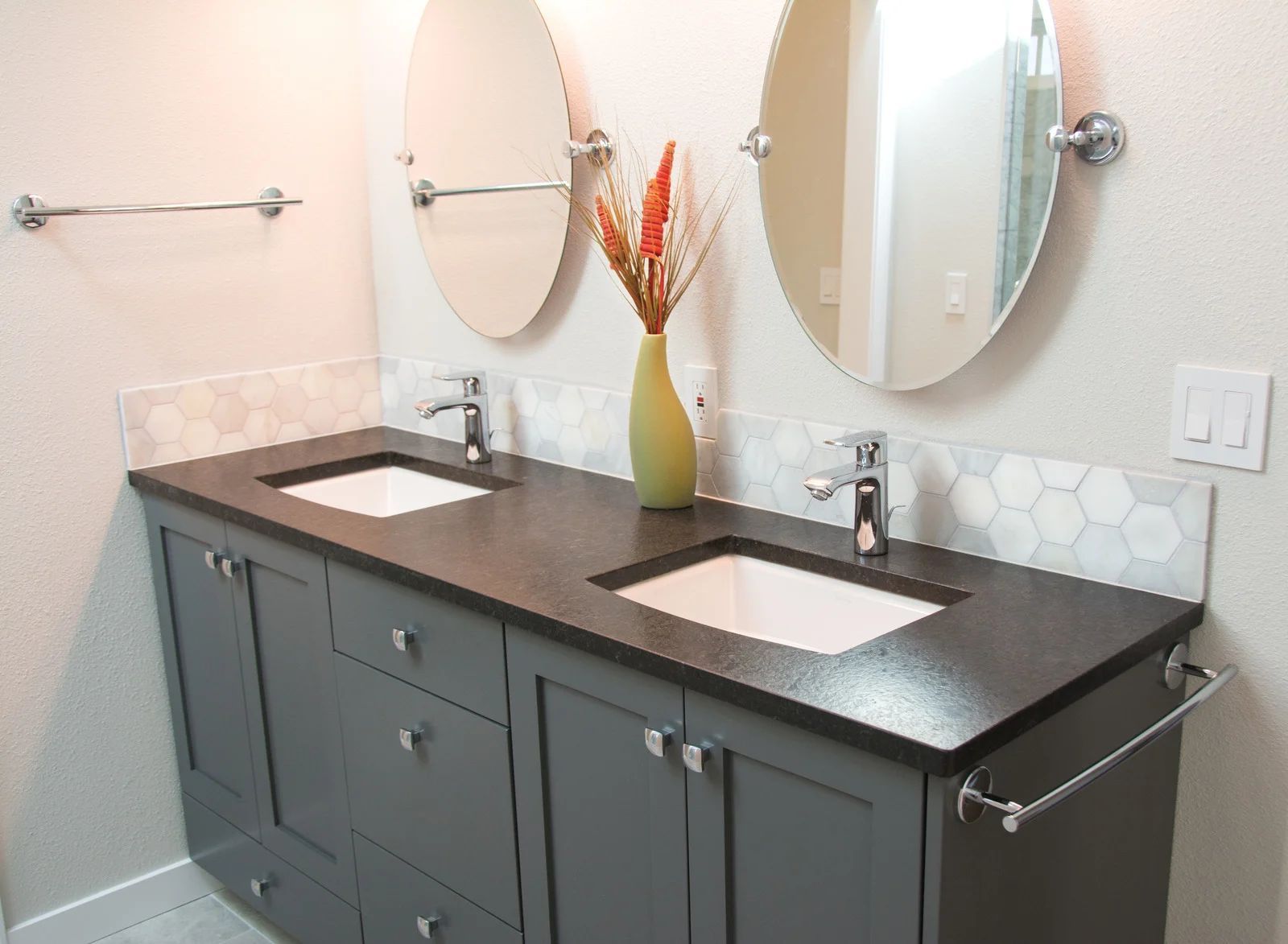 Gray double vanity with white sinks, oval mirrors, and floral arrangement in a bathroom.