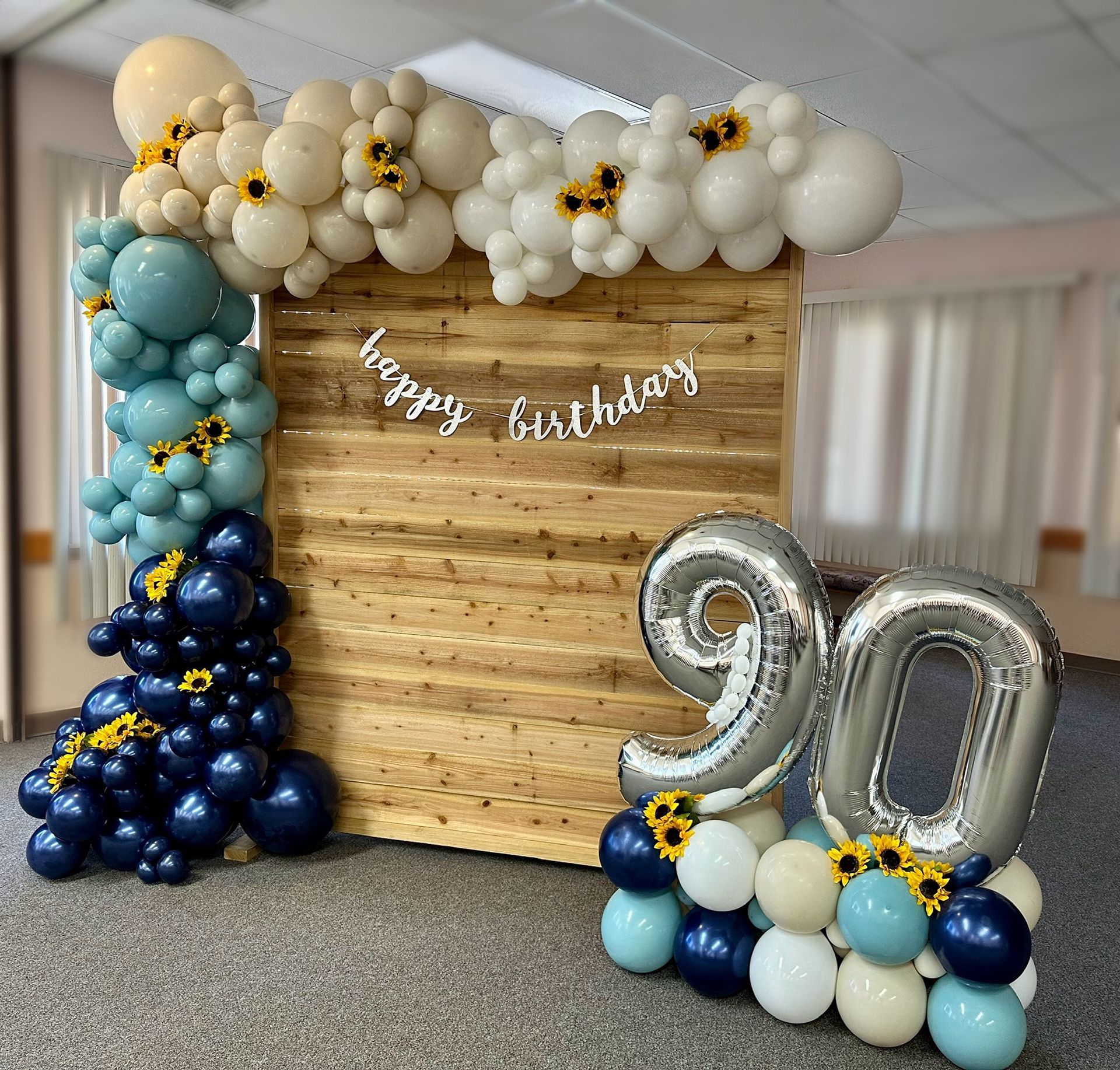 Birthday party setup with balloon arch, wooden backdrop, and silver 
