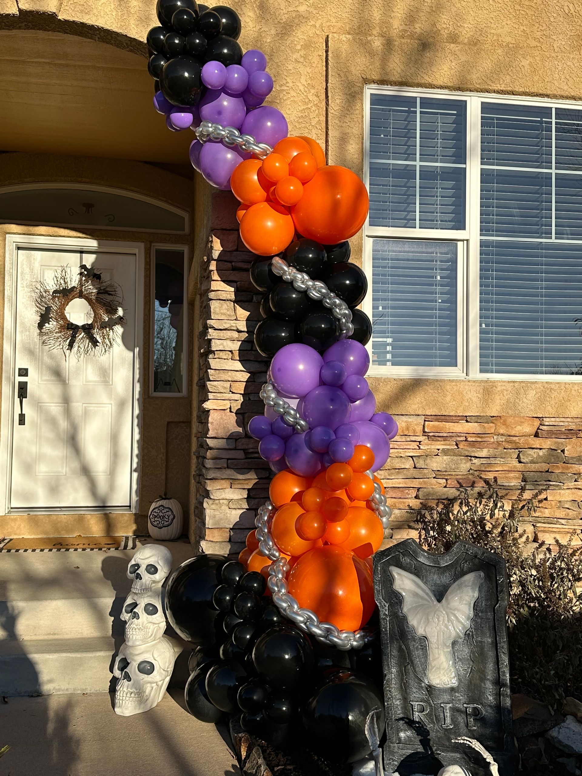 Halloween balloon arch on a porch with skulls and a decorative tombstone.