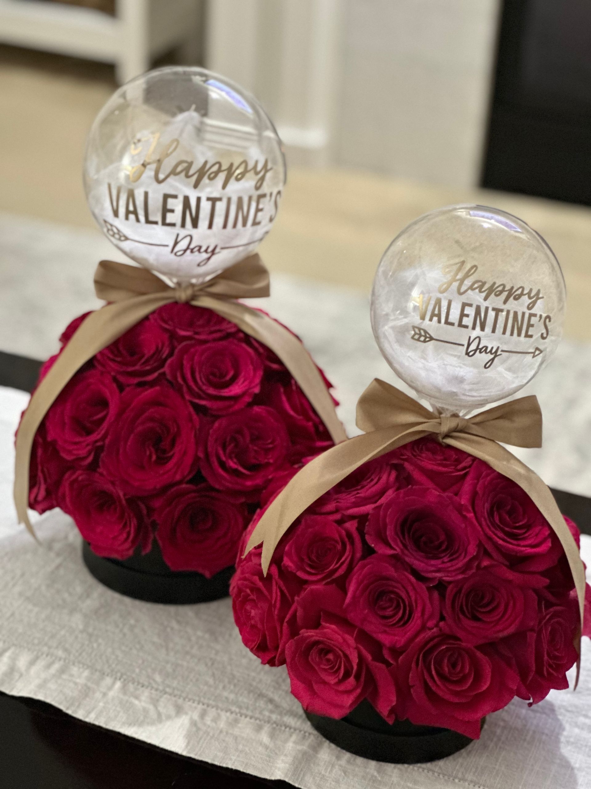 Two arrangements of red roses in black boxes, topped with balloons that say 
