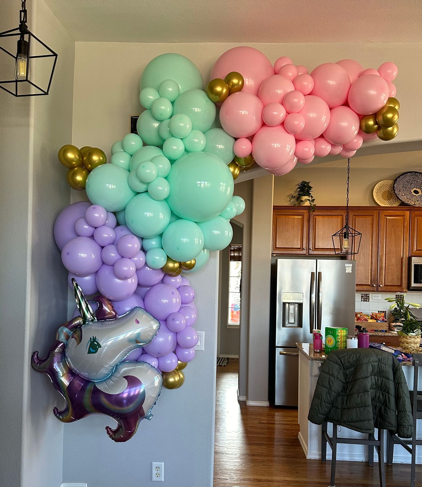 A colorful balloon arch with a unicorn attached. The balloons are pink, teal, gold, and purple. Inside a home.