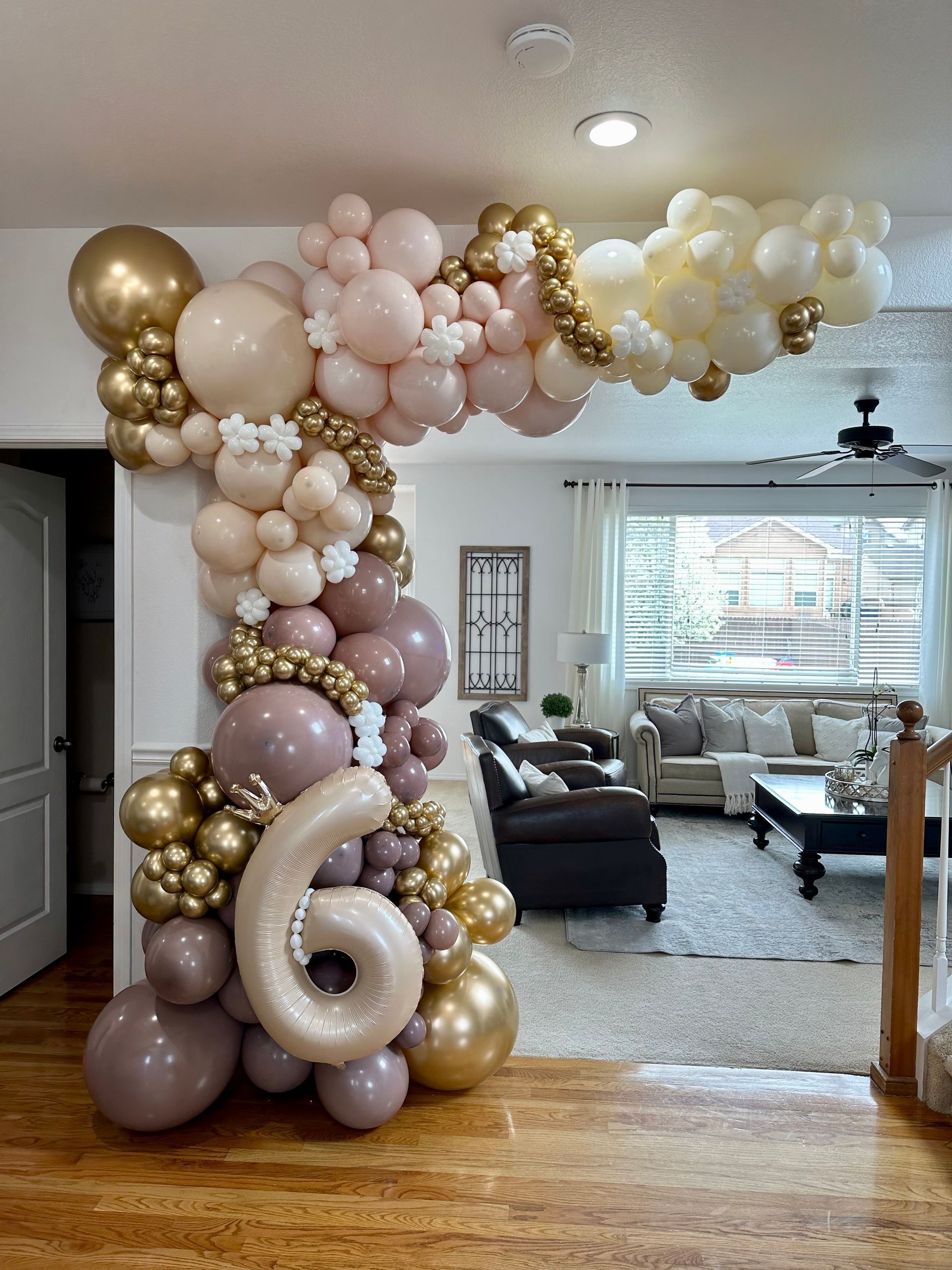 Balloon archway with gold, beige, and pink balloons frames a doorway; a 