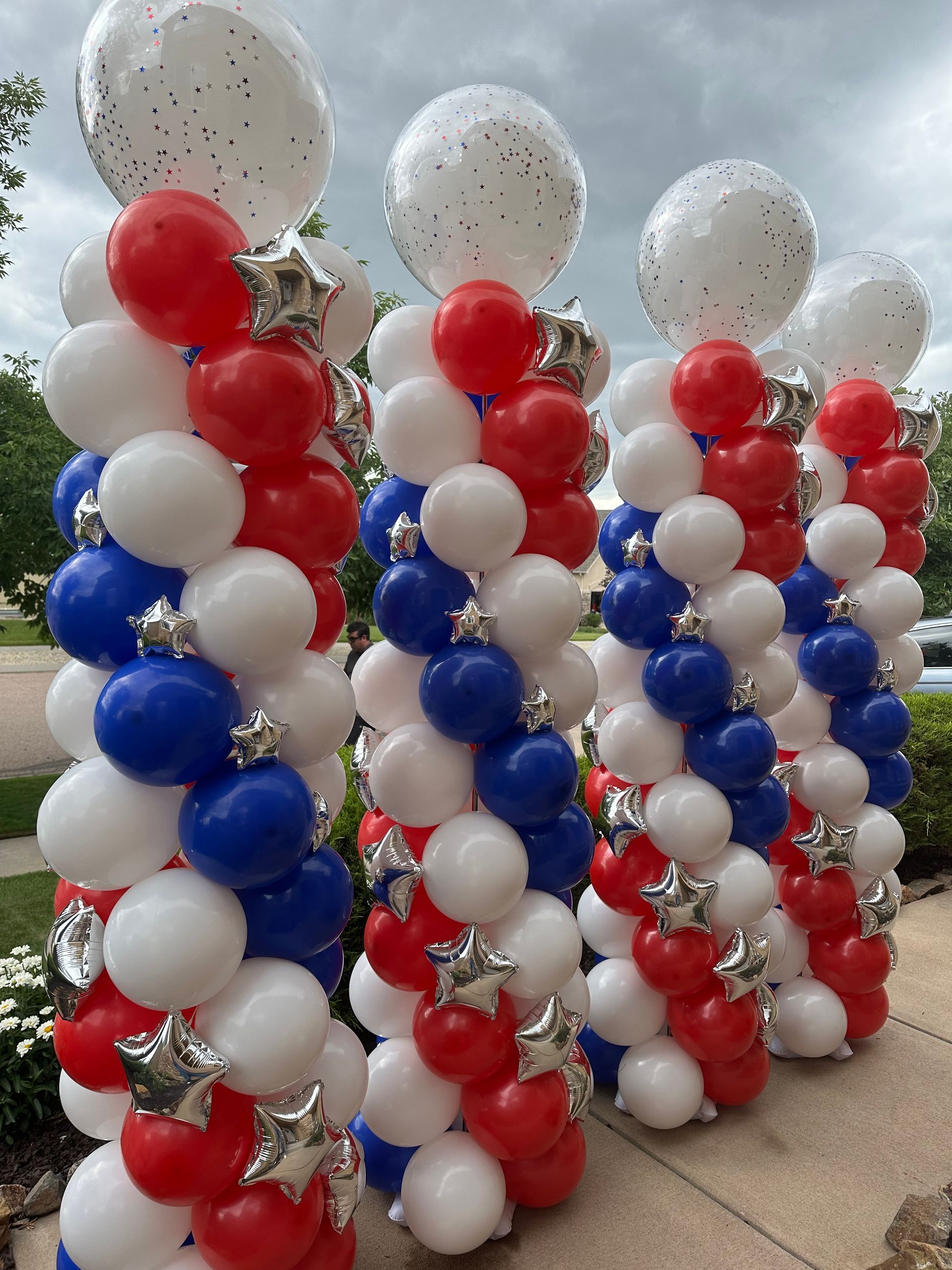 Red, white, and blue balloon columns topped with white confetti balloons, for a patriotic celebration.