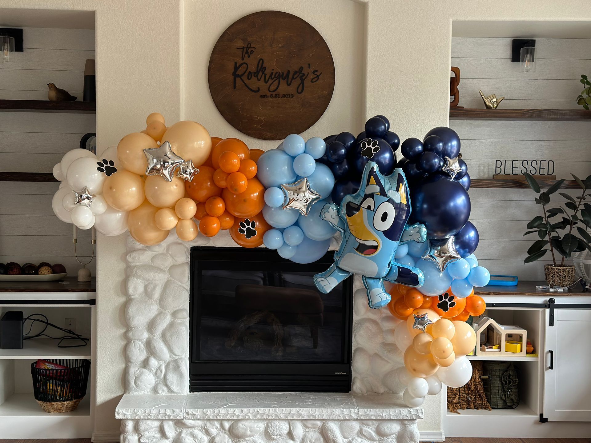 Balloon arch with Bluey, orange, blue, and tan balloons over fireplace.