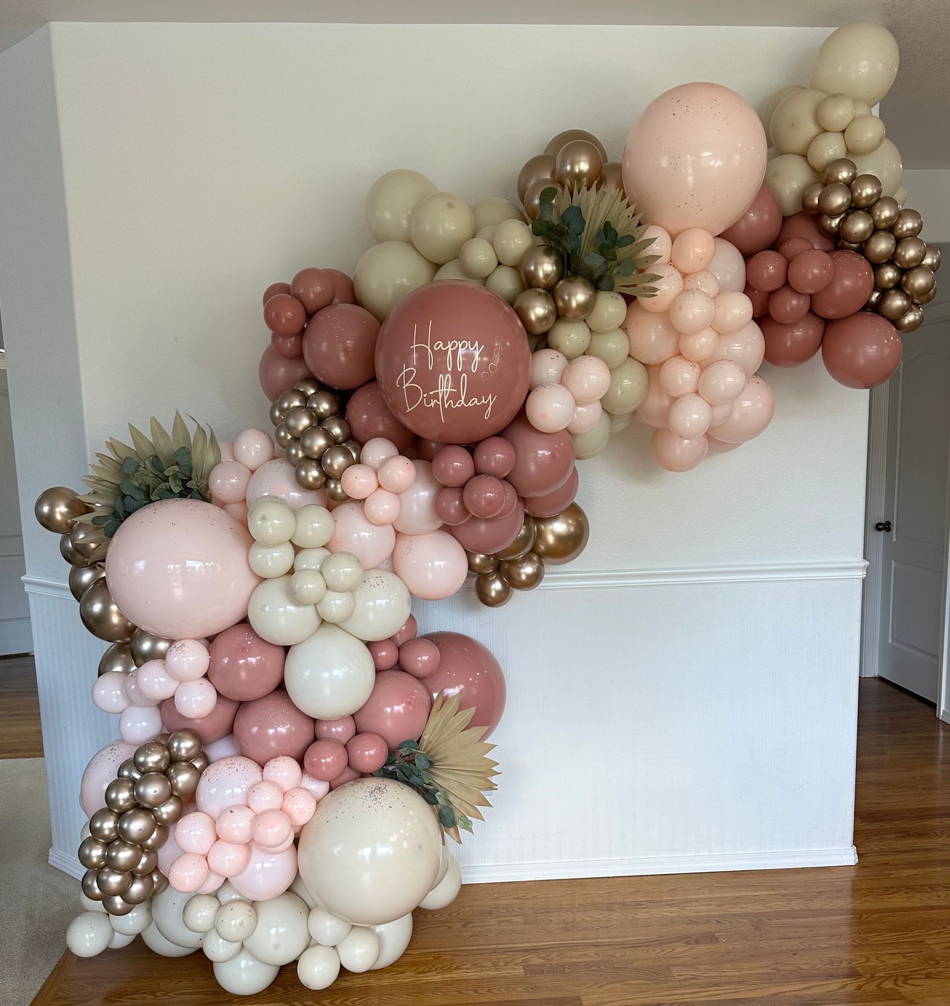 Balloon garland with pink, beige, and gold balloons on a white wall.