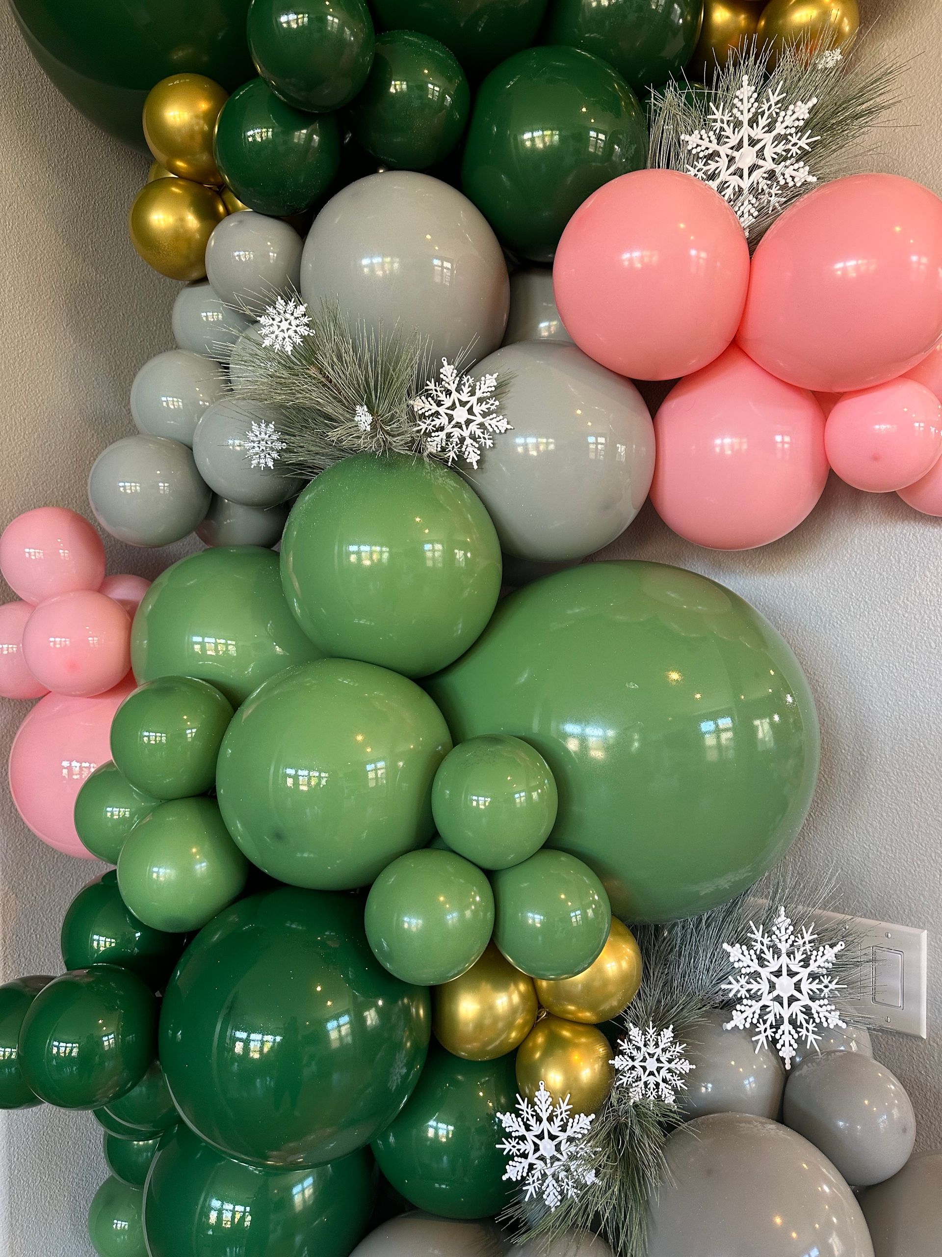 Balloon garland with shades of green, pink, gray, and gold, decorated with silver snowflakes.