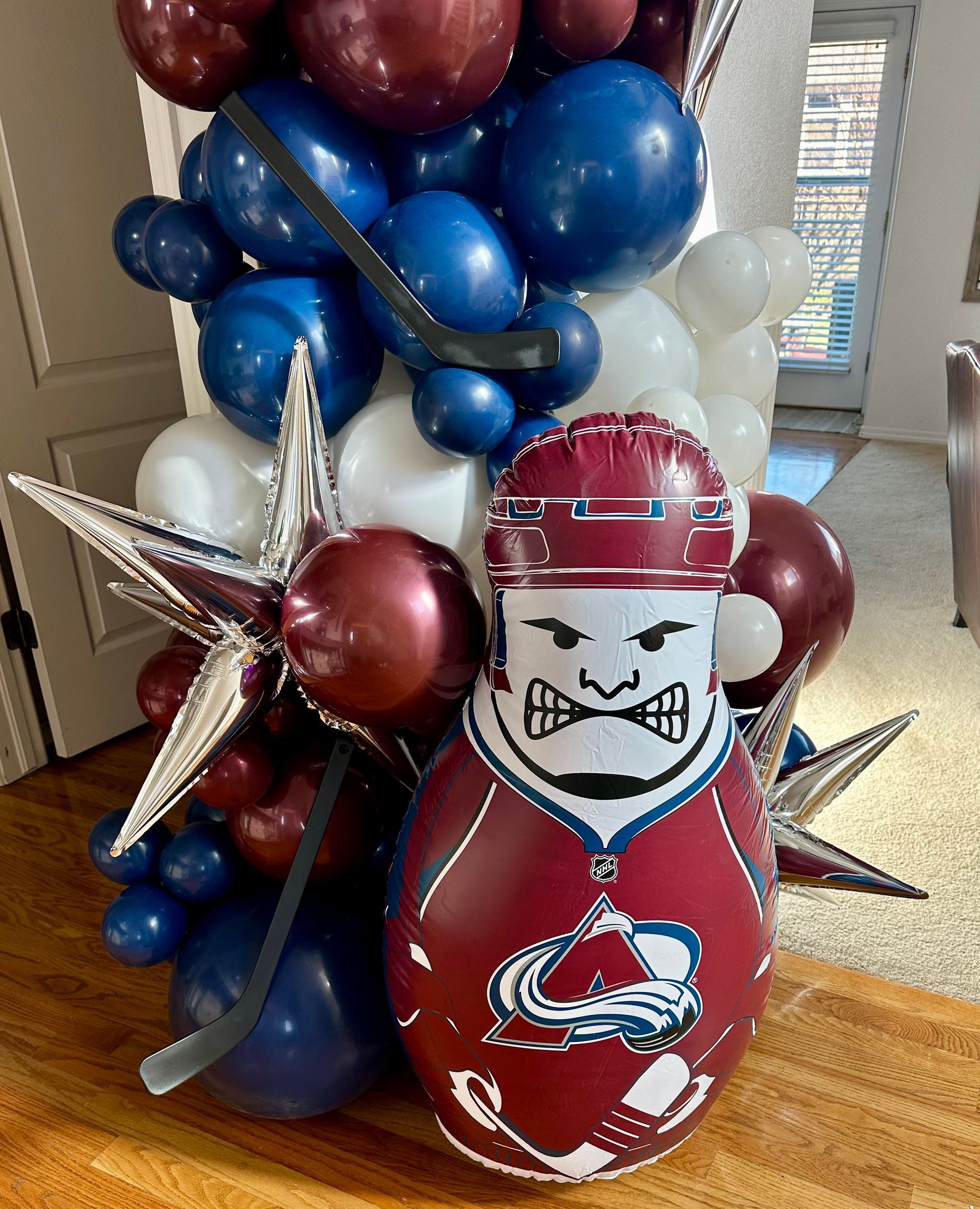 Colorado Avalanche-themed balloon display: burgundy and blue hockey player-shaped balloon with hockey stick, star balloons, and balloon column.
