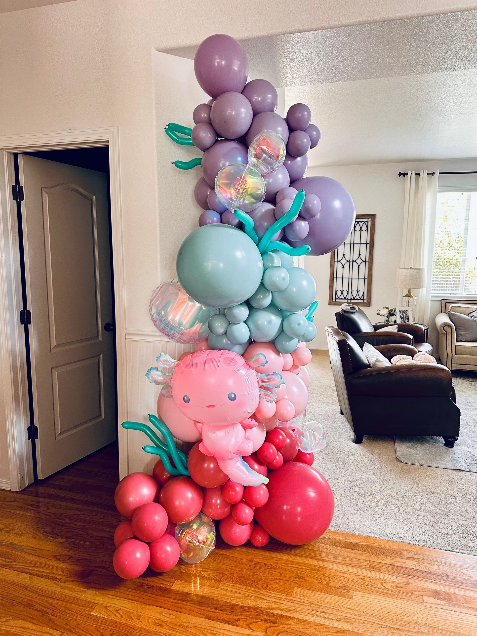 Balloon arch in shades of pink, red, and purple, featuring a seashell and sea creature theme, indoors.