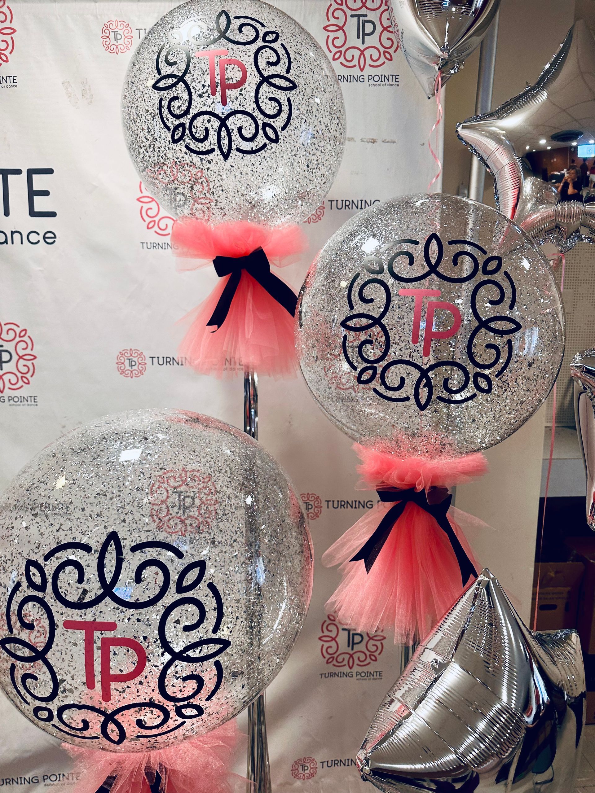 Glitter balloons with pink tulle skirts, black bows, and TP monogram. Silver star and diamond balloons.