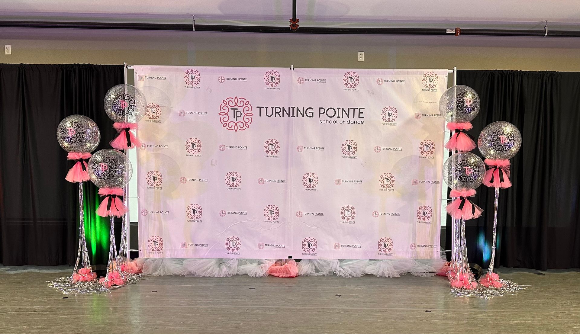 Event backdrop with pink logo, balloons, and black curtains.