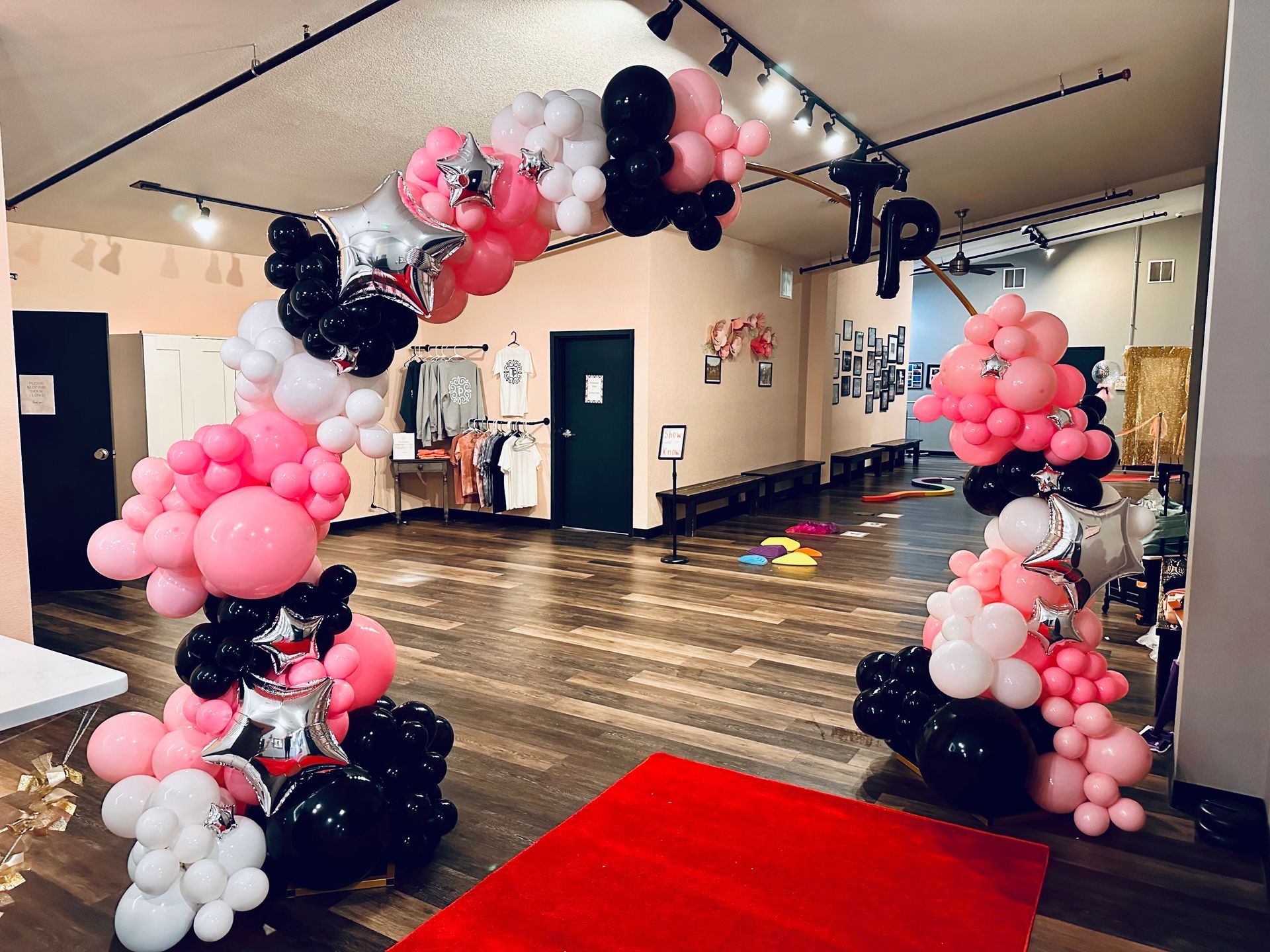 Pink, black, white balloon archway over a red carpet in a studio space.