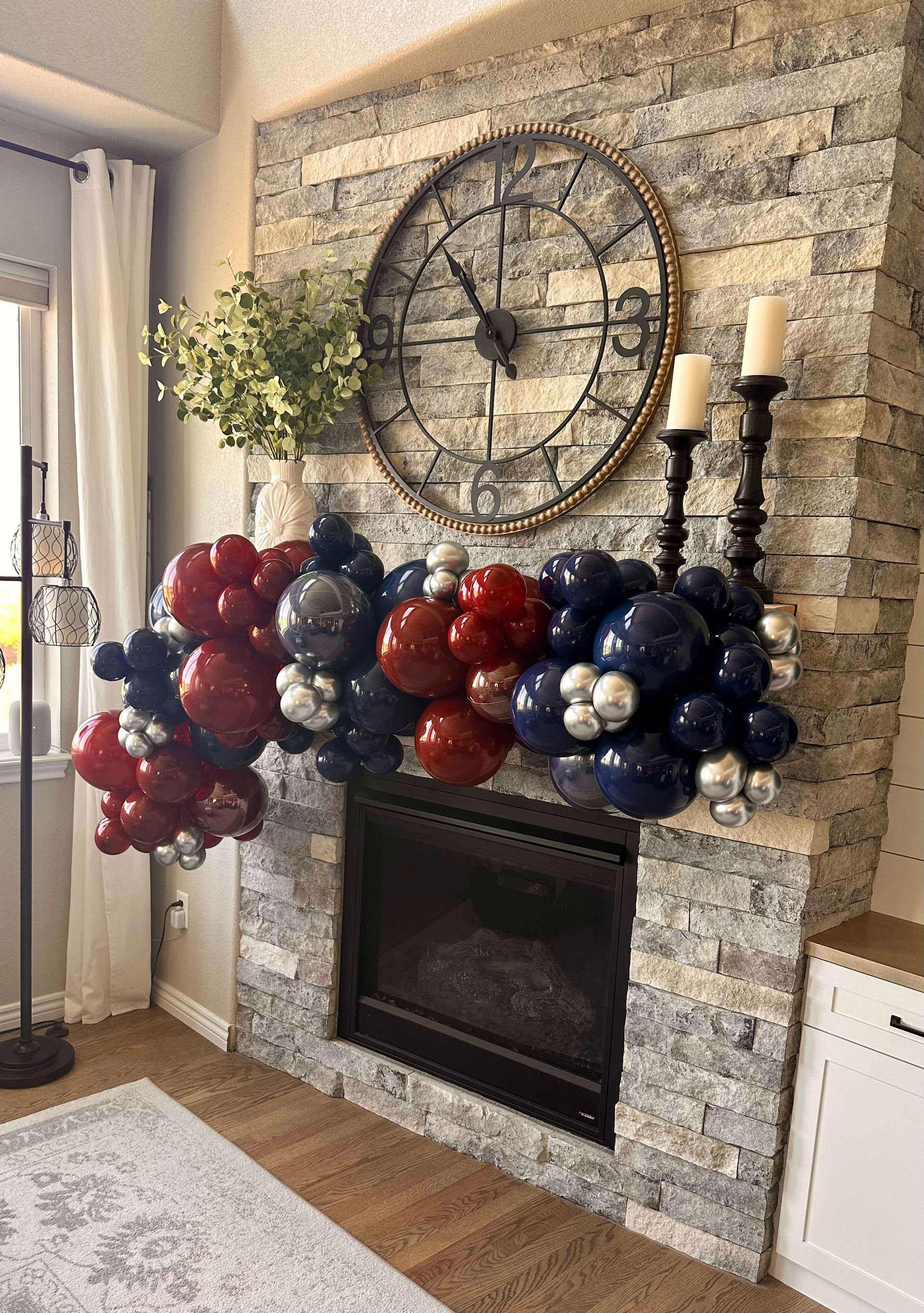 Fireplace decorated with red, silver, and blue balloons, candles, and a large clock.