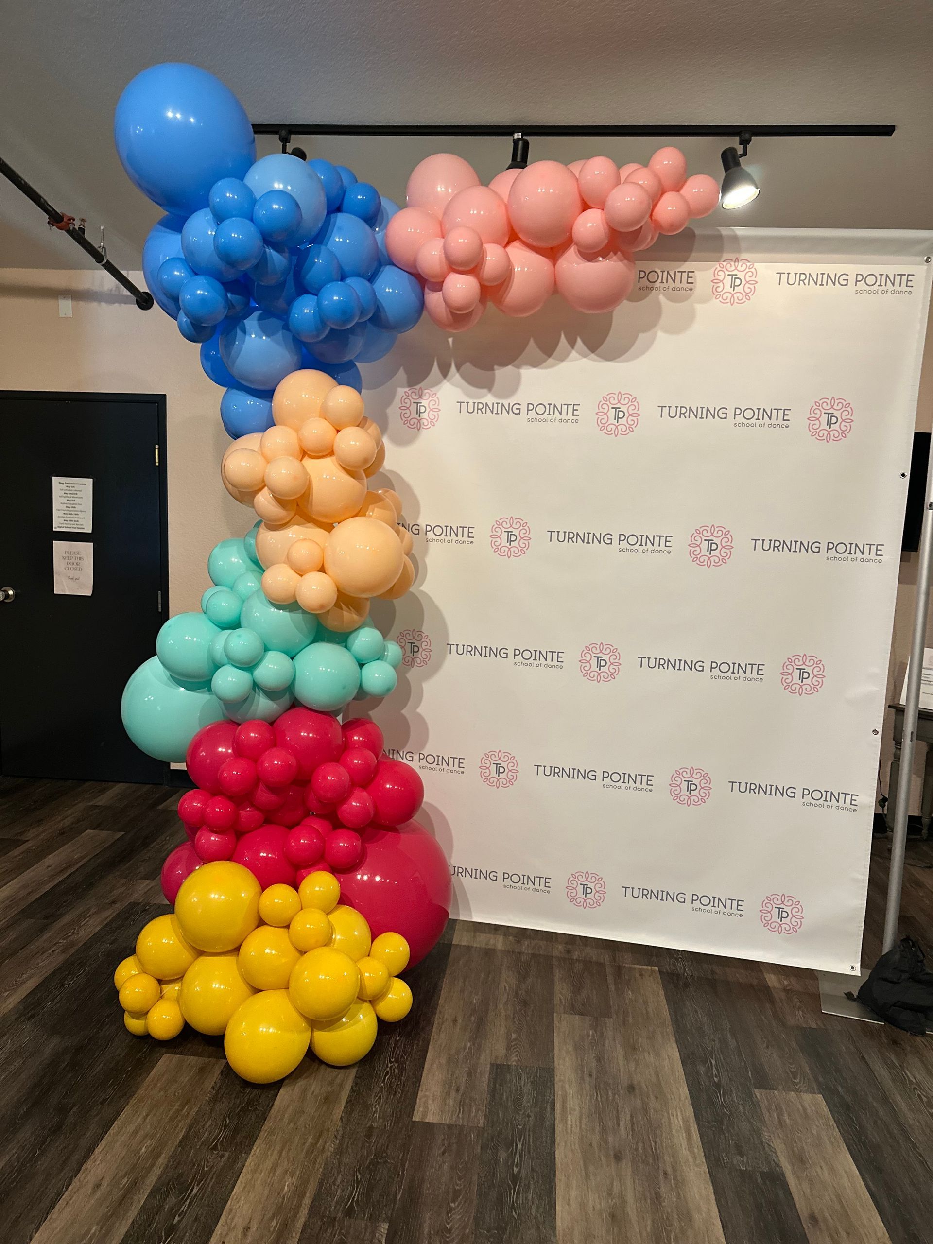 Colorful balloon arch with blue, pink, orange, teal, red and yellow balloons next to a white backdrop.