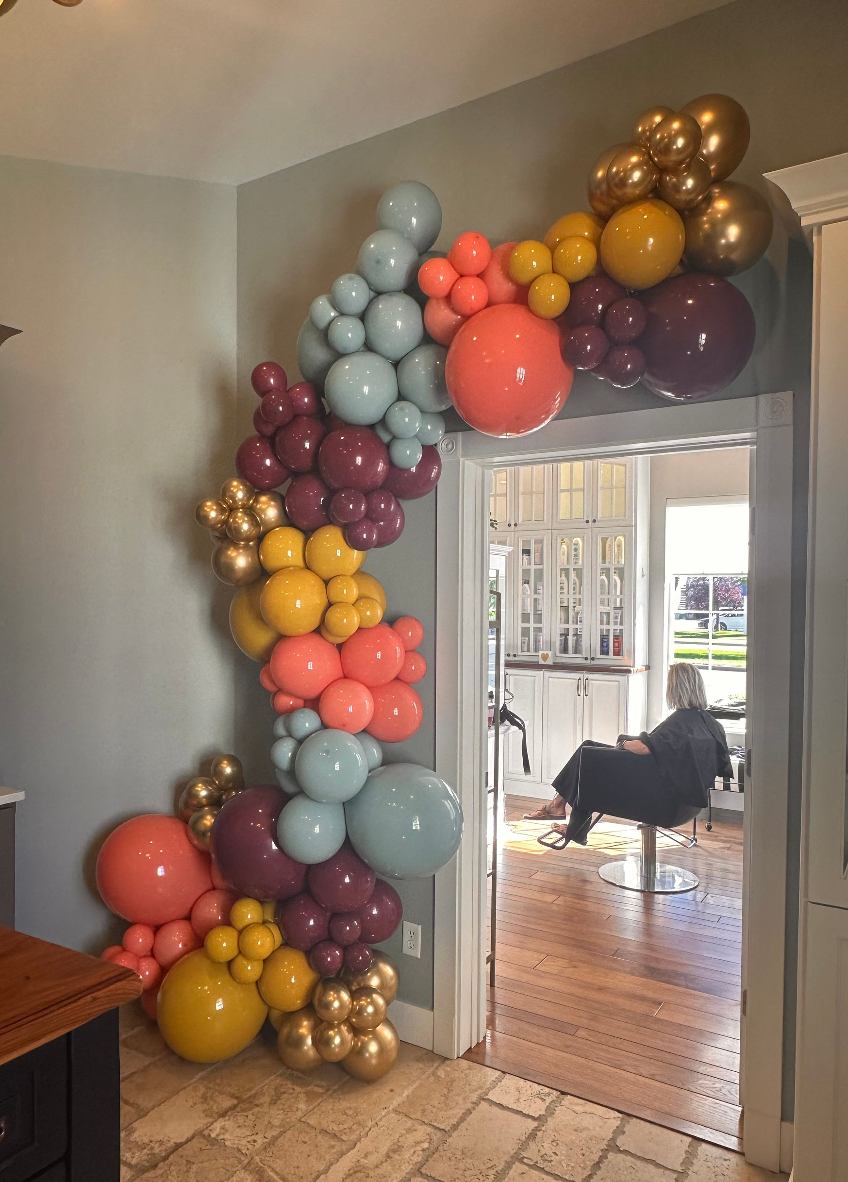 Arch of colorful balloons around a doorway: teal, gold, coral, and burgundy.
