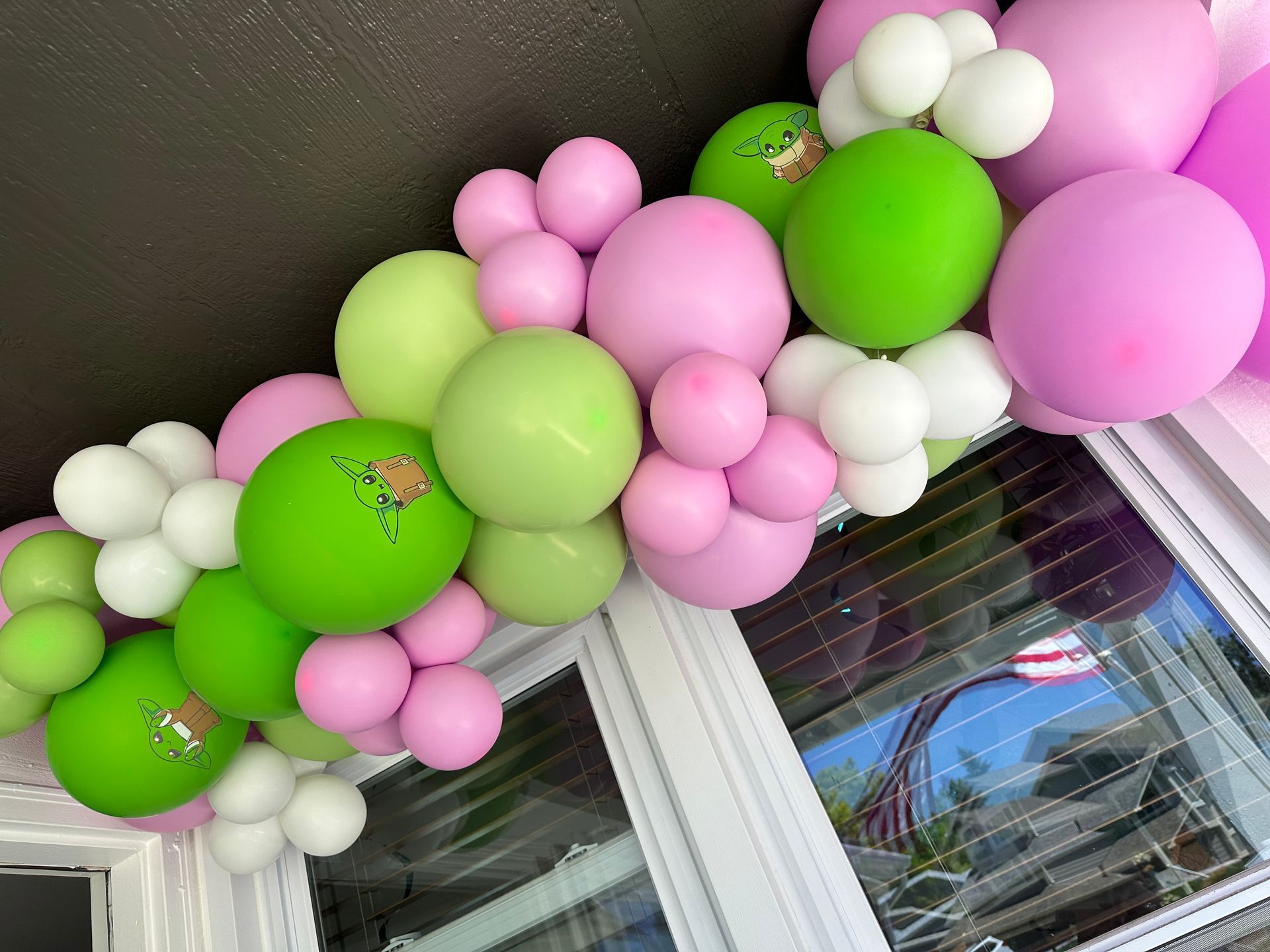 Balloons in shades of green, pink, and white forming an arch above a window.