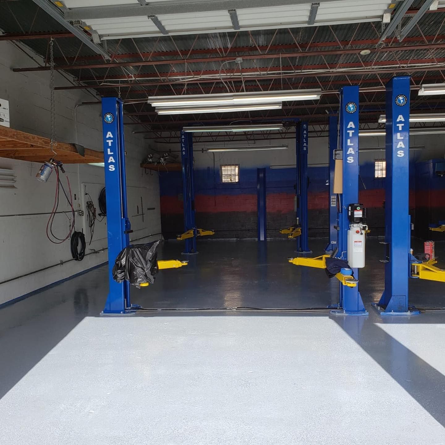 Empty auto repair shop with blue lifts, gray floor, and red/blue painted wall.