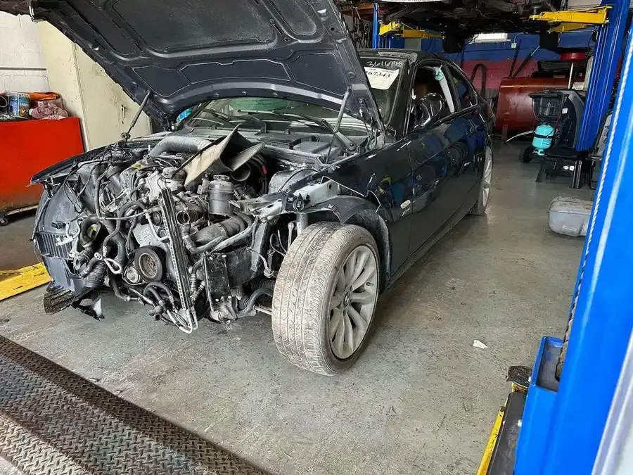 Damaged black car with hood open at a repair shop, front end heavily damaged.