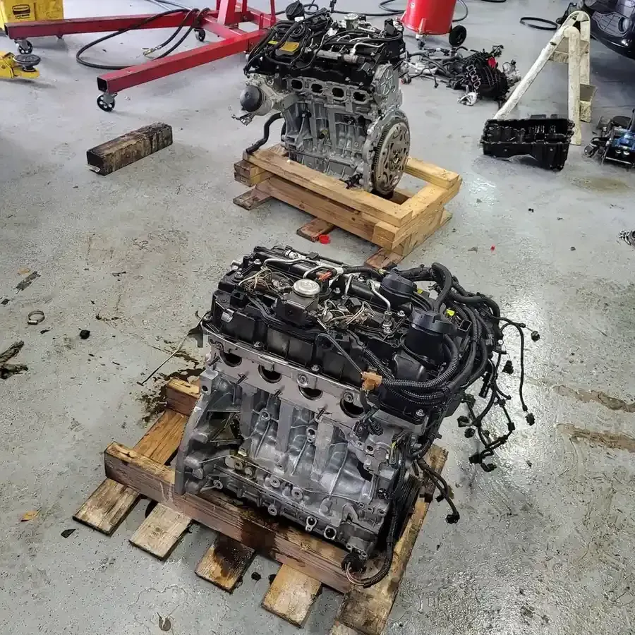 Two car engines on wooden pallets in a workshop, tools and parts scattered around.