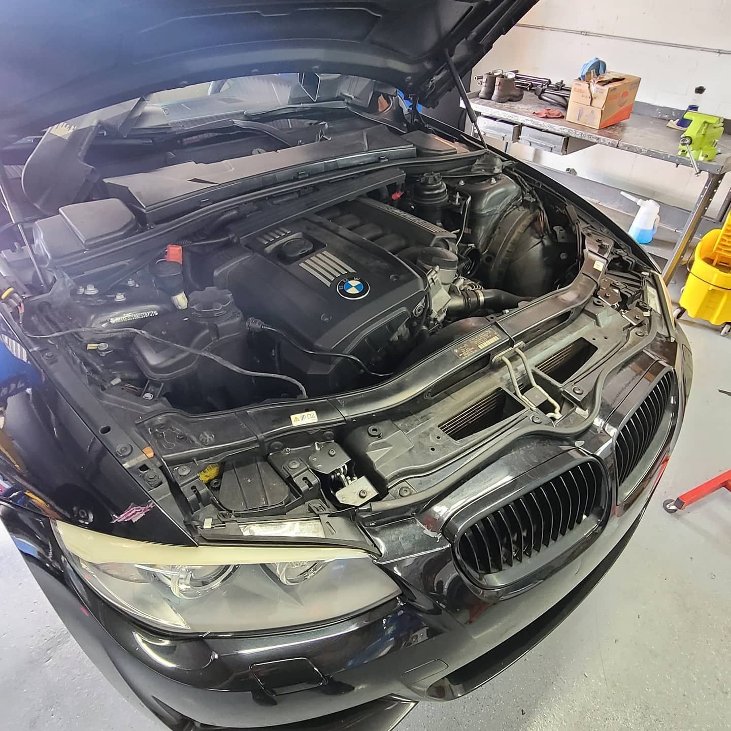 Black BMW car with hood open, engine visible in a shop setting.