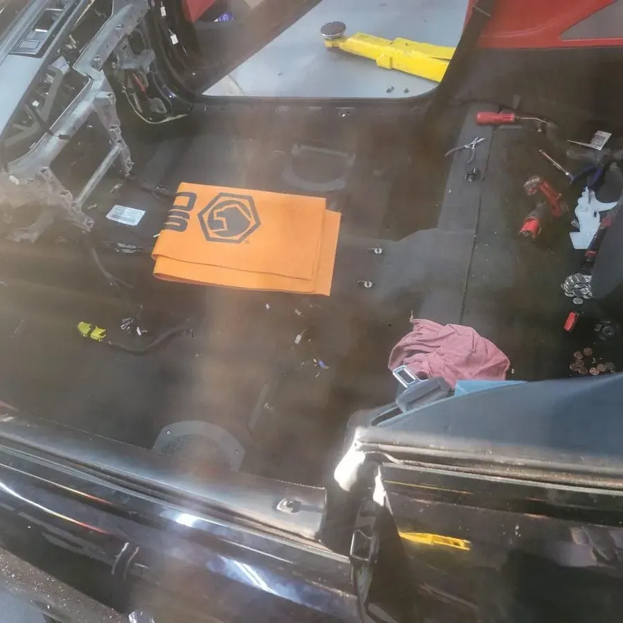 Interior of a car with seats removed. Orange sound dampening material sits on the floor. Tools and wiring are visible.