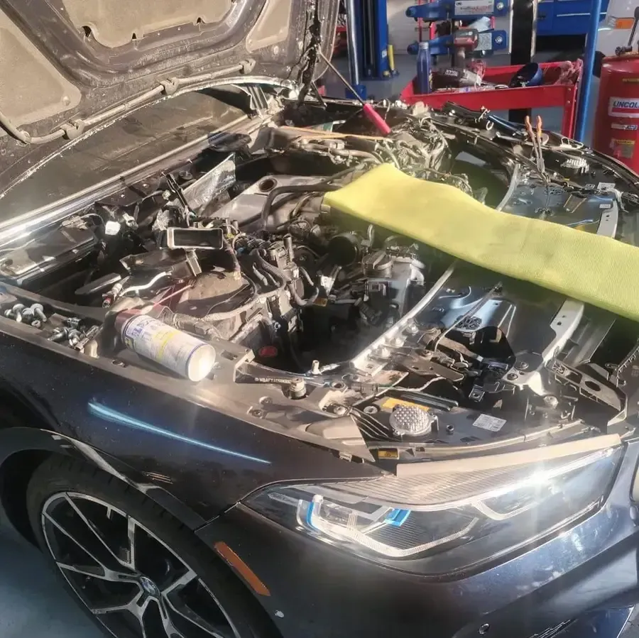 Car with open hood at an auto repair shop. Engine is visible, repair in progress, with tools and a cleaning cloth.