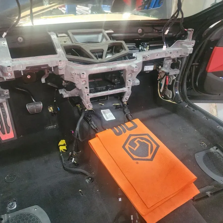 Car's interior disassembled, revealing dashboard frame, wiring, and floor. Orange towels on the floor.
