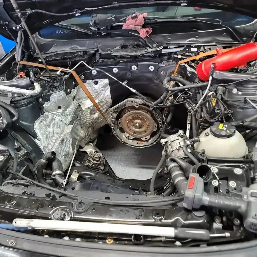 Car engine bay, partially disassembled. Visible are parts, tools, and silver insulation.