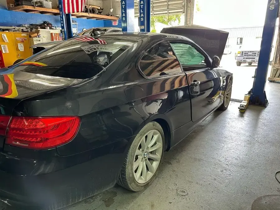Black BMW coupe in a garage, hood up, on a lift.