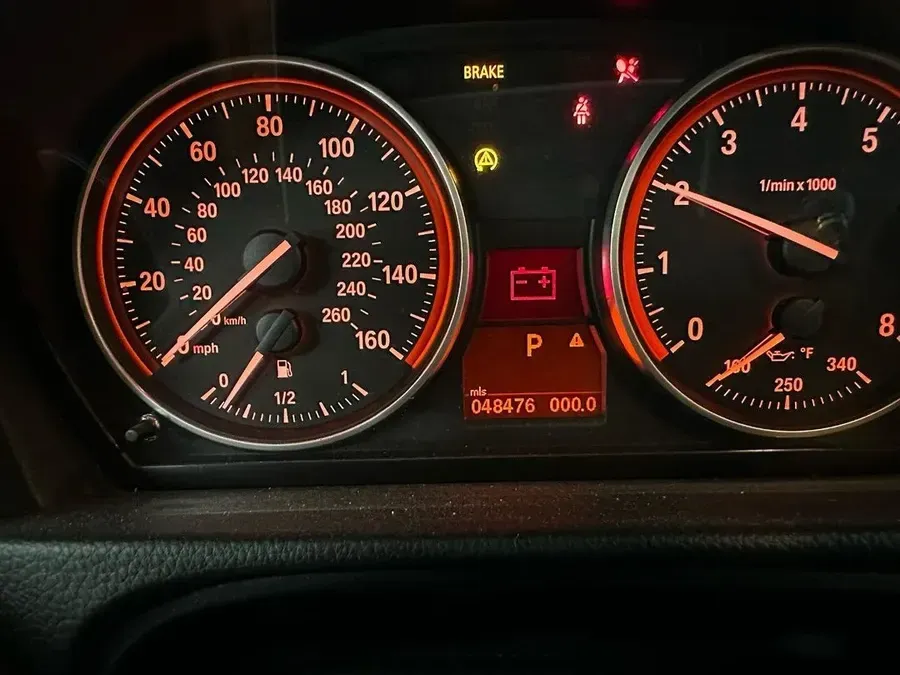 Car dashboard with speedometer, tachometer, and warning lights illuminated, including battery symbol.