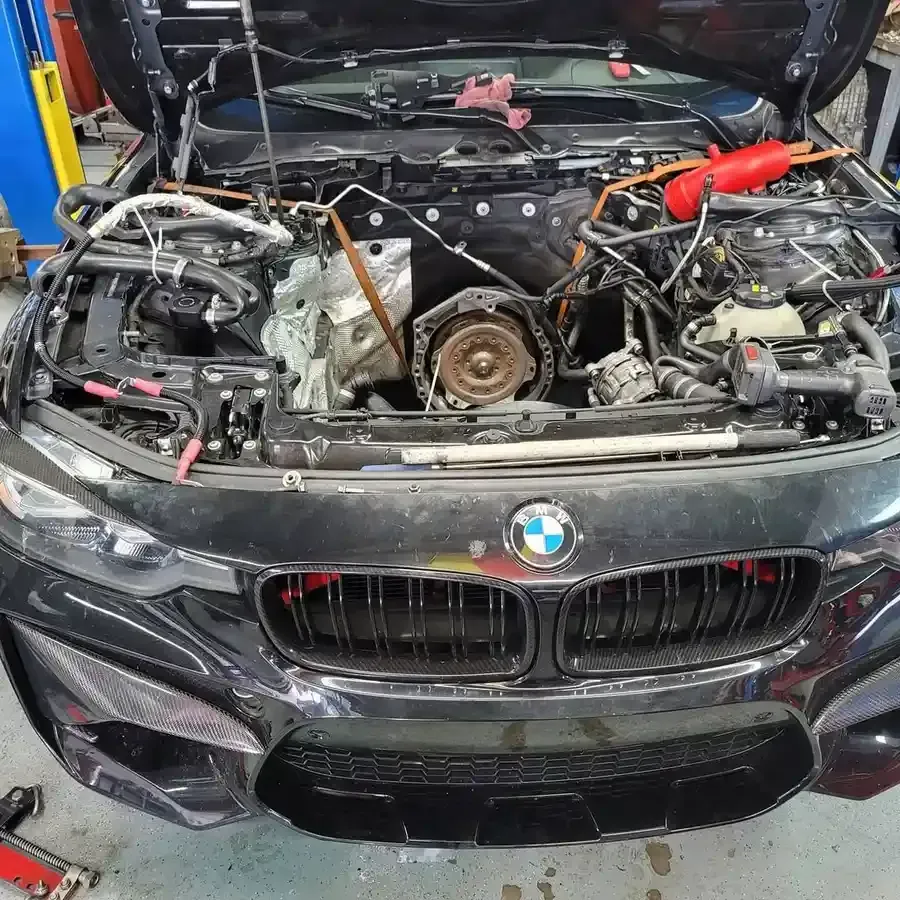 Black BMW with the hood open, revealing the engine components being worked on in a garage.