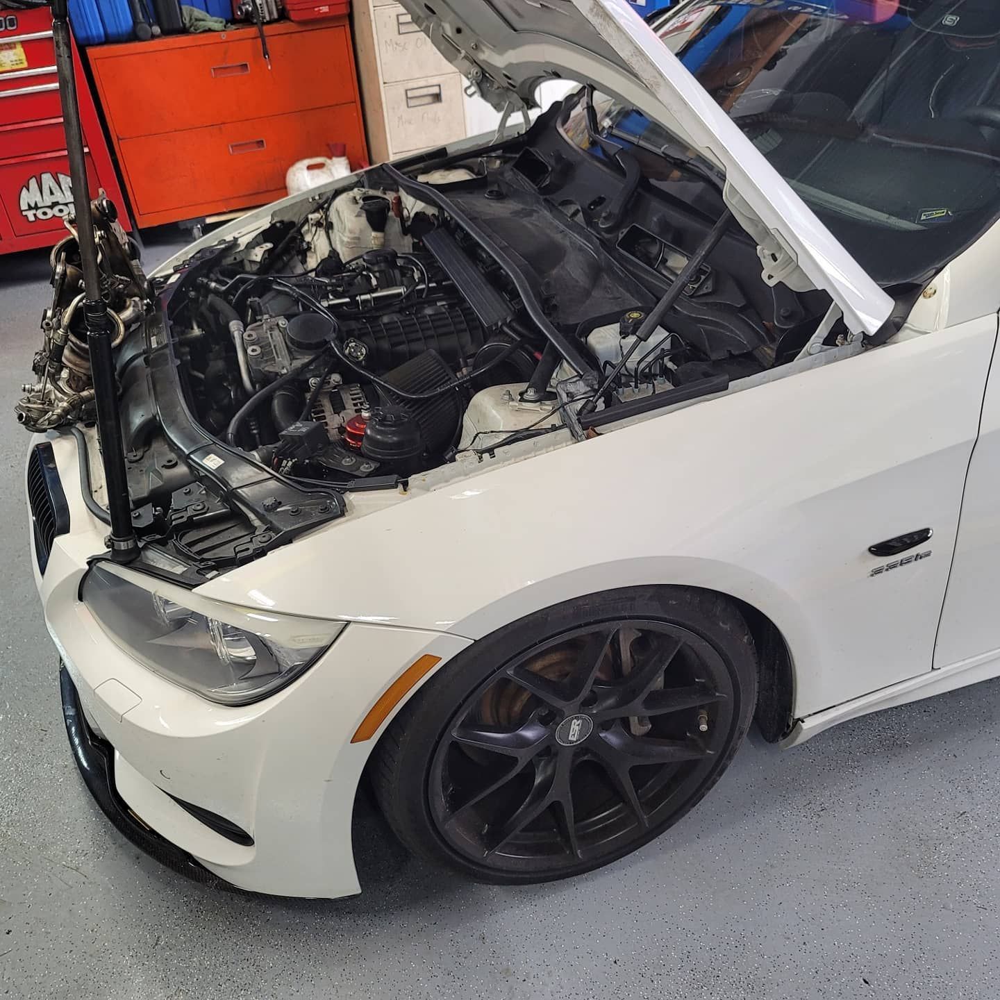 White car with open hood, engine visible, parked in a garage.