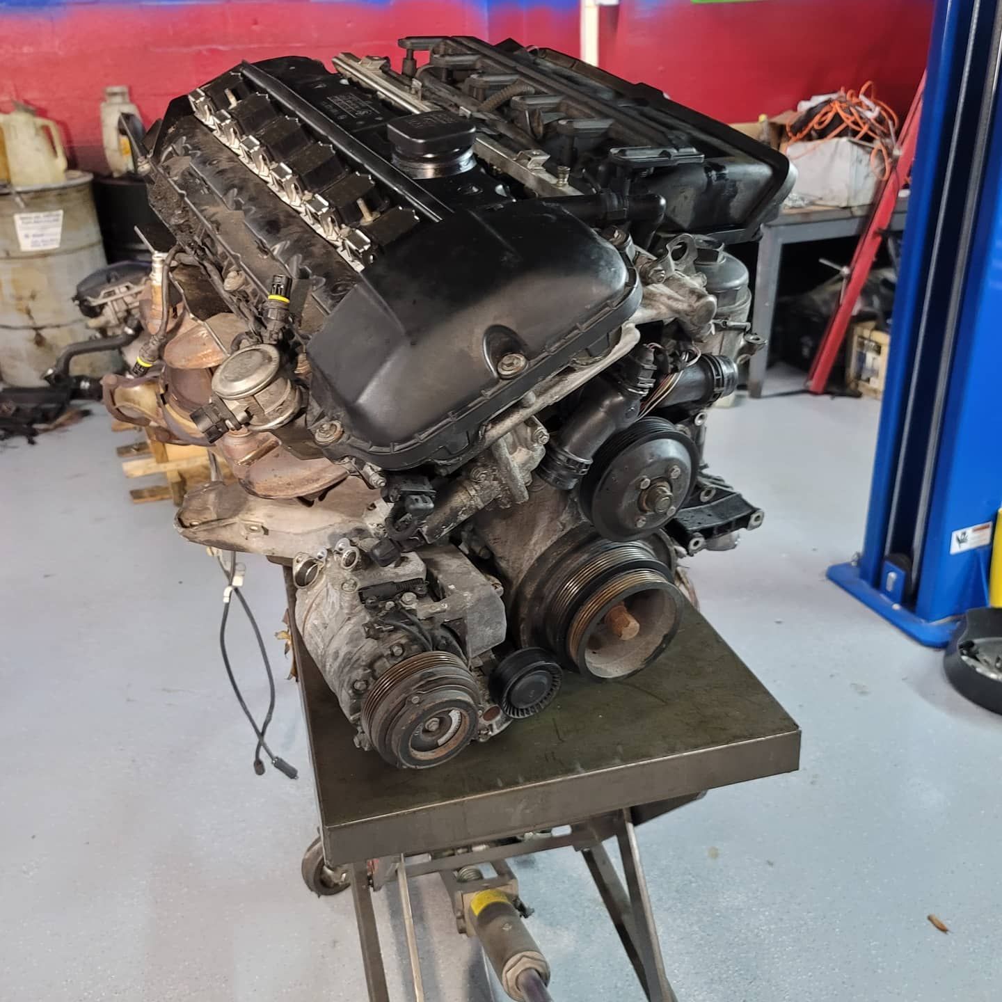 A car engine on a metal table in a workshop. It is black and has various components visible.