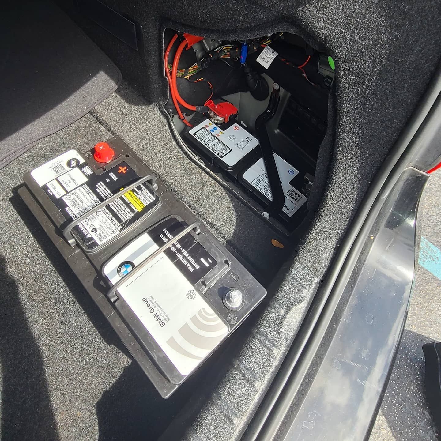 Car trunk interior with two car batteries visible. Black carpet and wiring are present.