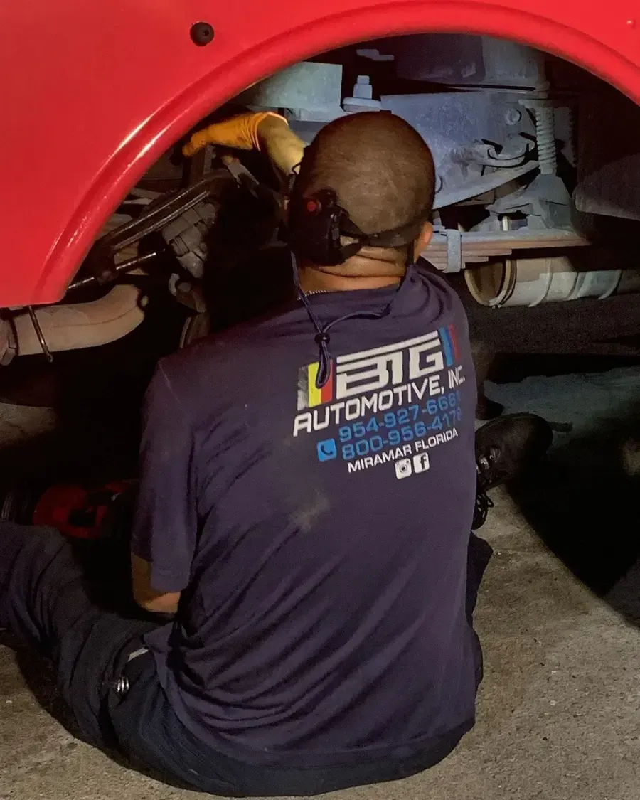Mechanic working under a red vehicle. He's wearing a blue shirt with 